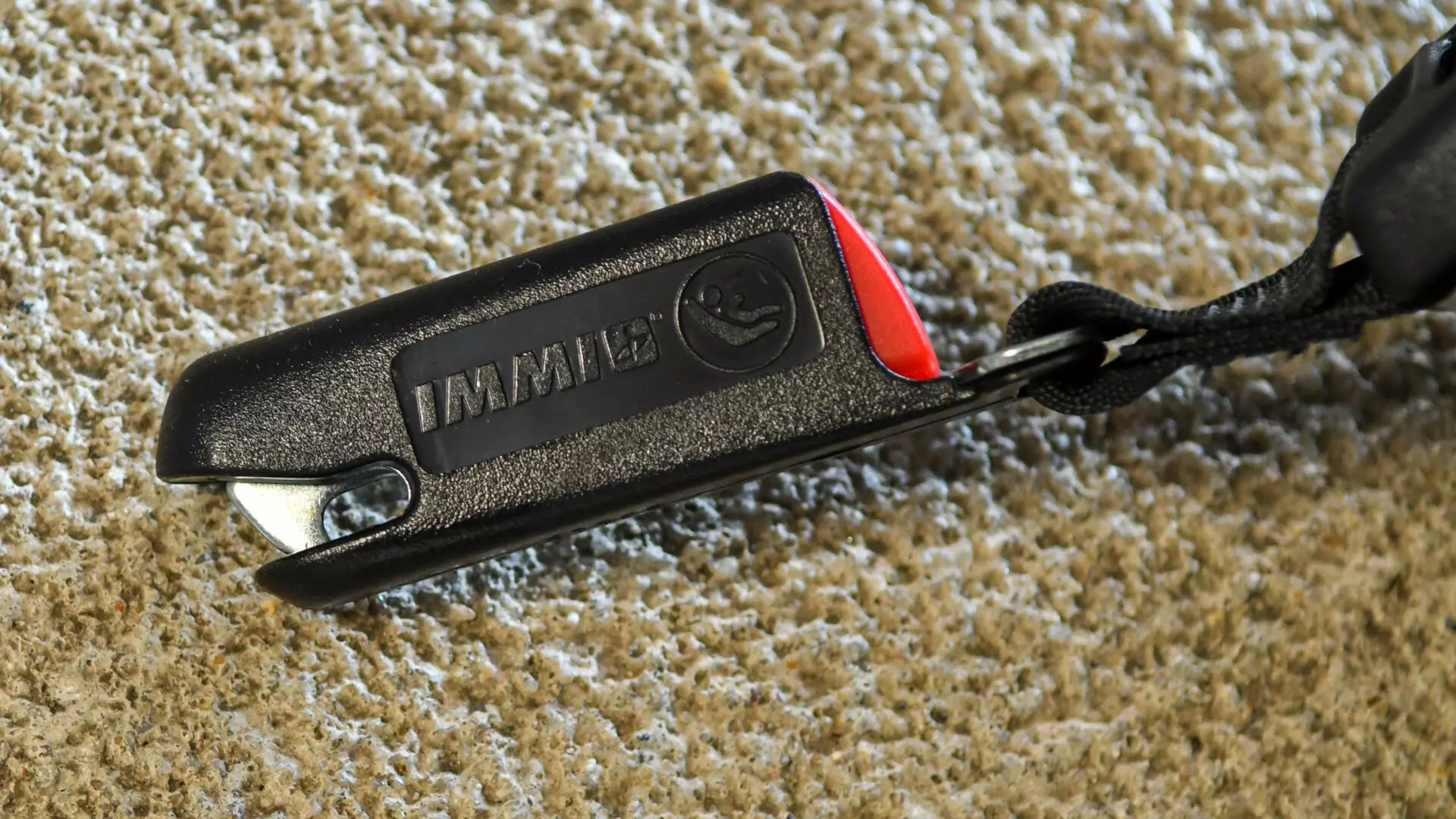 A zoomed-in image of an IMMI car seat hook placed outside on a textured sidewalk.