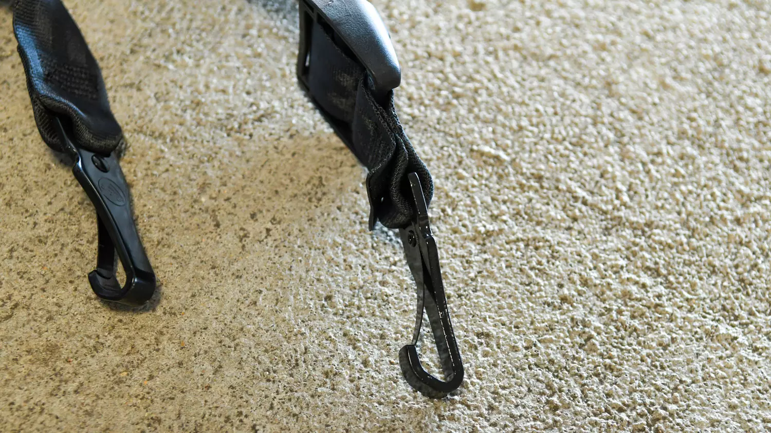 An image of two black car seat hooks placed outside on a textured sidewalk.